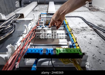 A male electrician works in a switchboard with an electrical connecting cable. Stock Photo
