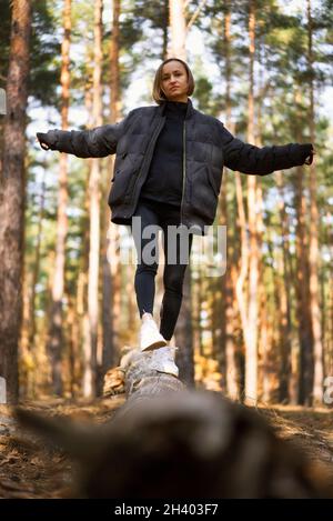 A girl walks on a log in a pine forest in autumn. Girl balancing on a log in the forest Stock Photo