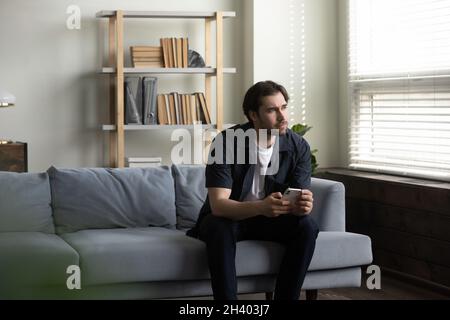 Thoughtful young handsome man holding smartphone in hands. Stock Photo