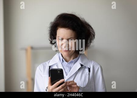 Happy middle aged female doctor using cellphone. Stock Photo