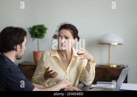 Concentrated middle aged woman talking with male colleague. Stock Photo
