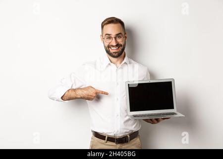 Professional manager showing webpage on laptop screen, pointing at computer, standing over white background Stock Photo
