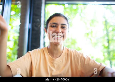 Headshot of indian woman sit on potdoor cafe waving hand looks to camera make video call chat use computer laptop webcam view, v Stock Photo