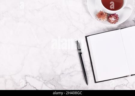 Empty open notebook, pencil and tea cup on side of marble table with copy space Stock Photo