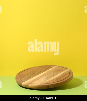 Round wooden kitchen pizza board on yellow-green background, utensils levitate Stock Photo