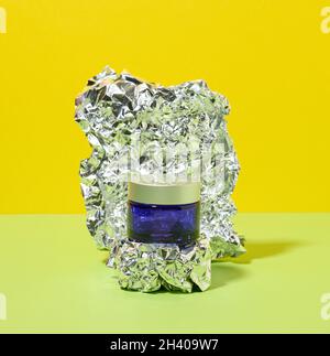 Blue glass jar with gray plastic lid for cosmetics on an abstract background with crumpled foil. Branding of cosmetic products c Stock Photo