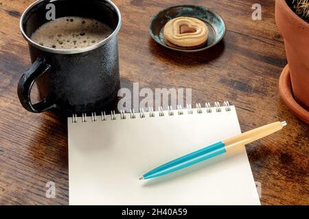 A blank notebook with a blue pen on a wooden desk, with a coffee mug Stock Photo