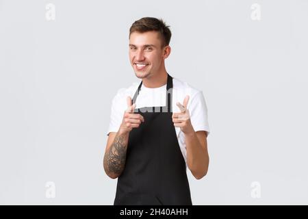 Employees, grocery stores and coffee shop concept. Cheeky handsome blond waiter, barista in black apron smiling broadly and poin Stock Photo