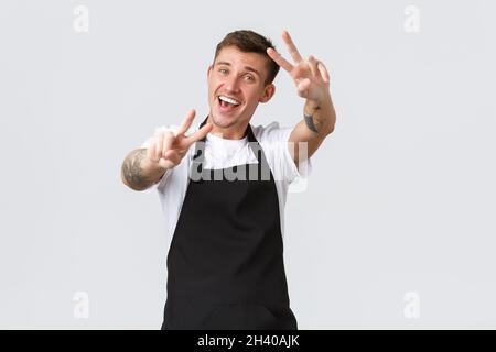 Employees, grocery stores and coffee shop concept. Friendly handsome hipster guy working in cafe, waiter send positive vibes, we Stock Photo