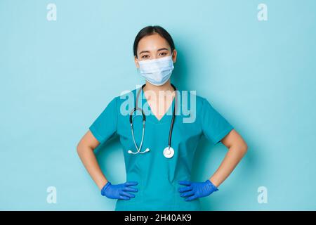 Covid-19, social distancing and coronavirus pandemic concept. Cheerful smiling asian female doctor, nurse in scrubs and medical Stock Photo