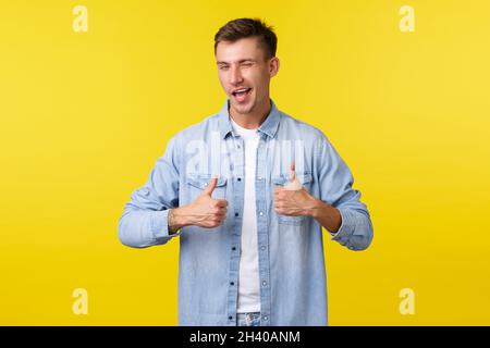 Handsome smiling young man showing thumbs-up and winking. Confident cute guy encourage make move, praising good job or saying we Stock Photo