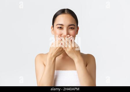 Beauty, cosmetology and spa salon concept. Beautiful asian woman in towel hiding lips, cover mouth with hands and giggle silly, Stock Photo