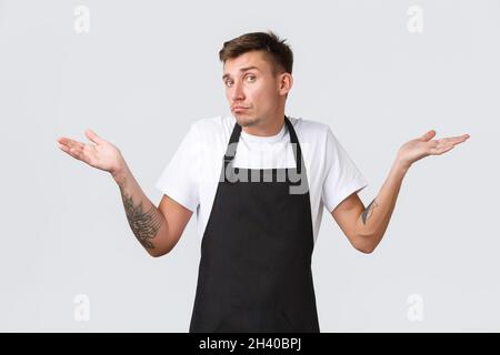 Employees, grocery stores and coffee shop concept. Clueless and indecisive handsome barista shaking head unaware and shrugging, Stock Photo