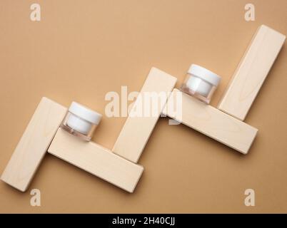 Empty white glass jar for cosmetics on a brown background and wooden blocks. Packaging for cream, gel, serum, advertising and pr Stock Photo