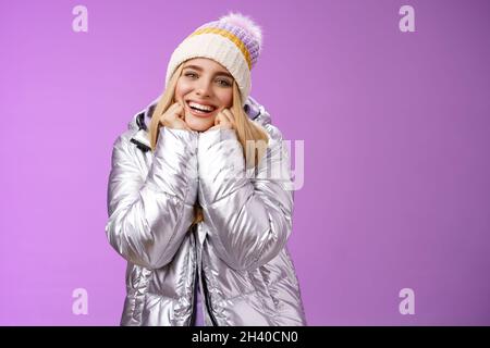 Delighted charming tender female in stylish cute hat silver shiny jacket lean chin hands smiling sighing enjoying watching lovel Stock Photo