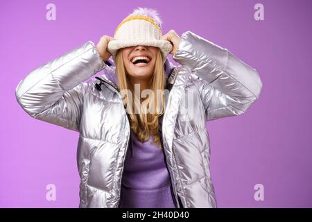 Delighted carefree charming happy young blond woman having fun hiding face pulling hat eyes smiling laughing joyfully enjoying w