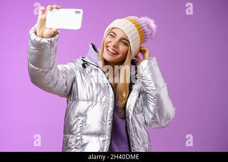Joyful carefree charming blond girl having fun wanna post pictures from ski resort vacation taking seflie holding smartphone mim Stock Photo