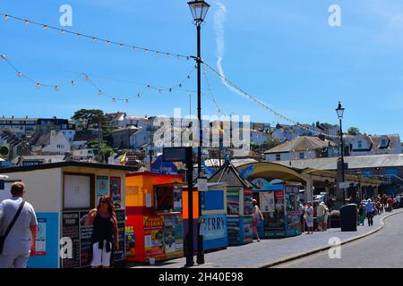Holidaymakers stroll along the quayside with it's colourful kiosks selling tickets for boat trips and fishing trips. Stock Photo