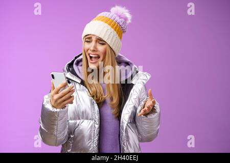 Bothered complaining dissatisfied cute blond girl yelling stupid smartphone standing unhappy recording audio message whining yel Stock Photo