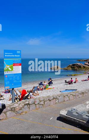 People enjoying sitting and playing on   the pebbly Breakwater Beach at the outside of Brixham Marina. Stock Photo