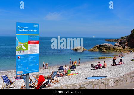 People enjoying sitting and playing on   the pebbly Breakwater Beach at the outside of Brixham Marina. Stock Photo