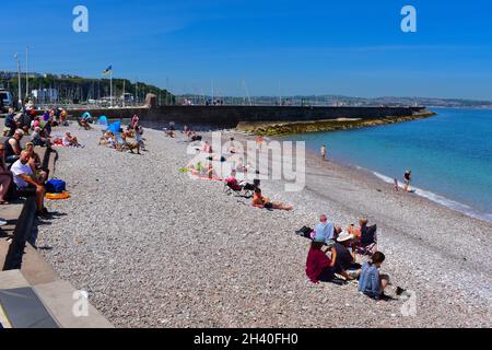 People enjoying sitting and playing on   the pebbly Breakwater Beach at the outside of Brixham Marina. Stock Photo