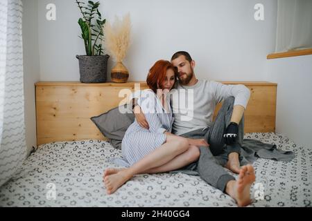 Tired thirty year old couple reasting on the bed, man hugging woman. He has a prosthetic bionic hand. Stock Photo