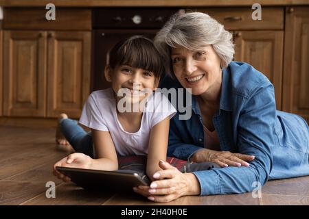 Happy grandma and cute gen Z granddaughter girl holding tablet Stock Photo