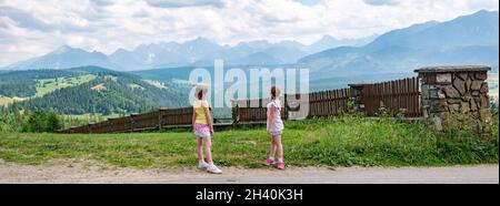 Two young children, elementary age girls standing in front of full Polish Tatra mountain range, high resolution panorama. Kids travel and exploration Stock Photo