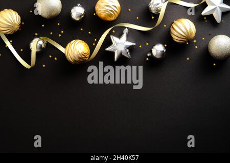 Luxury Merry Christmas and Happy New Year greeting card design. Golden and silver Christmas decorations and ribbon on dark black background. Flat lay, Stock Photo
