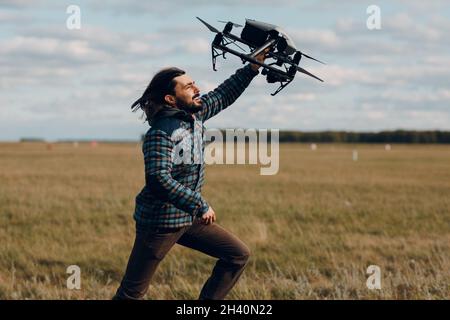 Man pilot holding quadcopter drone in hands at outside field. Stock Photo