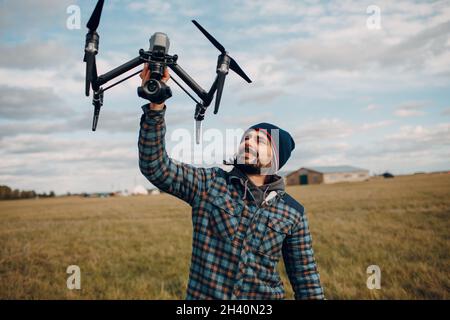 Man pilot holding quadcopter drone in hands at outside field. Stock Photo