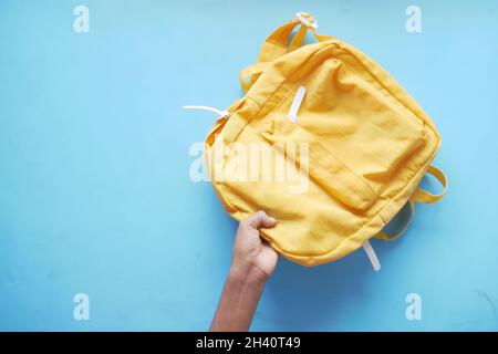 child boy hand holding a yellow backpack on blue  Stock Photo
