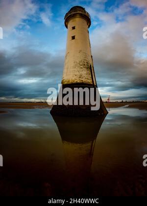 Lighthouse and its reflection in water on a sandy beach near Wallasey, Wirrall against a blue and cloudy sky. Stock Photo