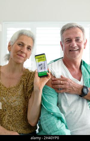 Smiling caucasian senior couple showing smartphone with covid vaccine passport on screen Stock Photo