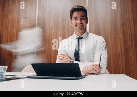 Businessman using laptop sit at table in office meeting background with walking people with motion blur. Business people man and Stock Photo
