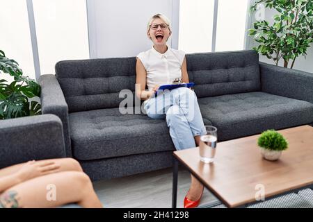 Young psychologist woman at consultation office angry and mad screaming frustrated and furious, shouting with anger. rage and aggressive concept. Stock Photo