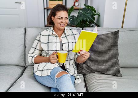 Middle age hispanic woman reading book drinking coffee at home Stock Photo