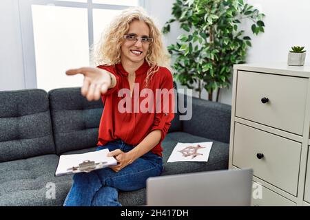 Middle age psychologist woman at consultation office smiling cheerful offering palm hand giving assistance and acceptance. Stock Photo