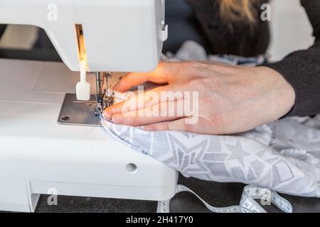 Female hands are sewing at home using a sewing machine closeup. Horizontally. Stock Photo