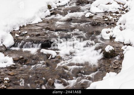 Small waterfall of cold water flow among the stones covered with snow Stock Photo