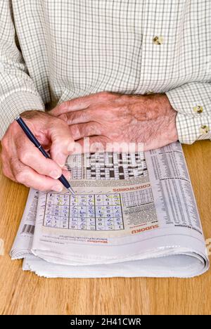 Vertical close up of an elderly gentleman doing the "Sudoku" puzzle in his daily newspaper. Stock Photo