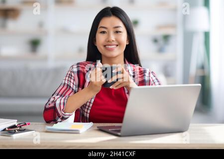 Remote Job. Smiling Asian Freelancer Woman Posing At Desk In Home Office Stock Photo