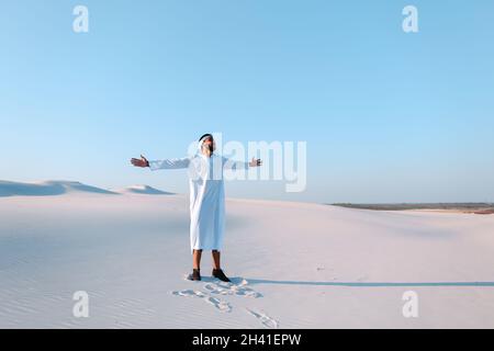 Happy Arab man walks in middle of white desert and enjoys life on hot summer day. Stock Photo