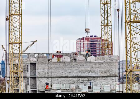 Bricklayer workers in safety orange vests and hard hats make walls of white silicate bricks on a construction site of a big residential house. Stock Photo