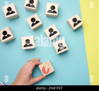 Female hand holds a wooden cube with a magnet and wooden cubes with little men, recruiting for a strong team. Open vacancies in Stock Photo