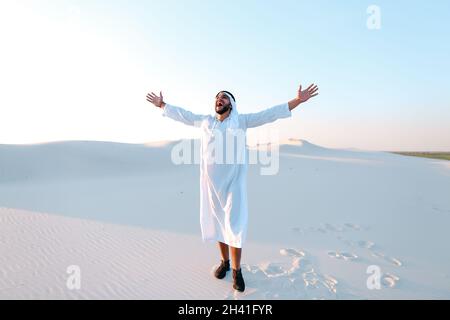 Happy Muslim man looks through banknotes and beside himself with joy, standing in center of sandy desert on warm, hot day. Stock Photo