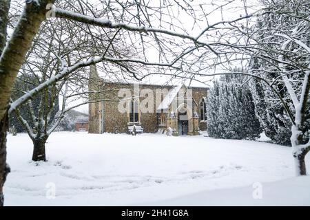 All Saints church in the small village of Sutton in the British countryside, it is totally covered in deep snow during a rare snow storm in the UK Stock Photo