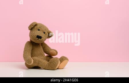 Brown teddy bear with patches sits on a white table, pink background Stock Photo