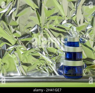 Blue glass jar with gray plastic lid for cosmetics on an abstract background with crumpled foil. Branding of cosmetic products c Stock Photo